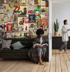 a woman sitting on a couch in front of a wall covered with posters