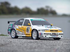 a yellow and white car parked on top of a gravel covered field next to a body of water