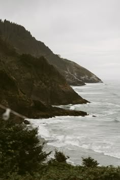 an ocean view with waves crashing in to the shore and trees on the cliff side