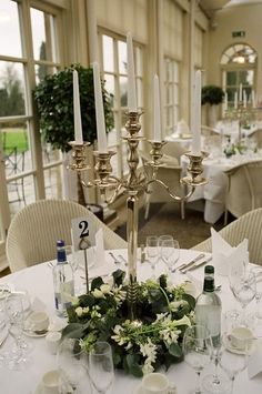 a centerpiece with candles and flowers on a table in a room filled with tables