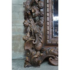 an ornate wooden mirror on the wall next to a brick wall with a reflection in it