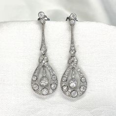 This lovely pair of earrings is Edwardian inspired, featuring intricate details in handcrafted platinum. Old mien cut diamonds are set along the drop of the earrings, surrounding the center diamond. The total approximate weight of these earrings is 2.00 carats. ✦ EARRING SPECIFICATIONS: Ring Material: Platinum Ring Era: Edwardian Era Stones: Diamond ✦ WHAT COMES IN YOUR SHIPMENT: - Your Engagement Ring - Quality Ring Box - Jewelry Cleaner - UGL Certificate ✦ WHY SHOP WITH US: - We've been in bus Luxury Platinum Diamond Earrings Hallmarked, Luxury Hallmarked Pear-shaped Diamond Earrings, Exquisite Pierced Diamond Earrings For Formal Occasions, Exquisite Diamond Pierced Earrings For Formal Occasions, Classic Hand-set White Gold Diamond Earrings, Classic Hand Set Diamond Earrings, Classic Hand Set White Gold Diamond Earrings, Classic Handset White Gold Diamond Earrings, Platinum Pear-shaped Diamond Earrings For Formal Occasions