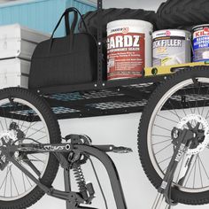 two bikes are parked next to each other in a garage with paint cans on the rack