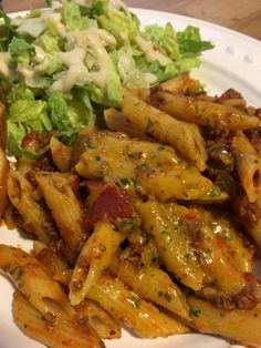 pasta with meat and sauce on a white plate next to a side of lettuce