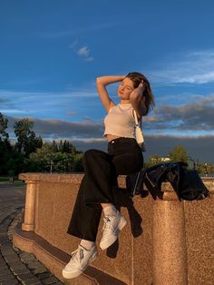 a woman is sitting on a wall with her hand on her head