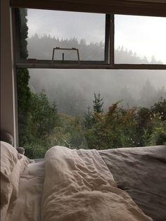 a bed sitting in front of a window next to a forest filled with lots of trees