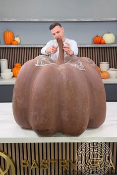 a man sitting in front of a giant pumpkin on top of a white countertop