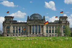 a large building with flags flying in front of it on a sunny day and green grass