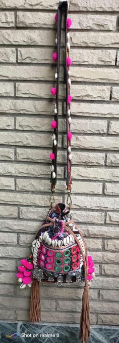 a purse hanging on the side of a brick wall with beads and tassels