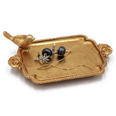 a pair of earrings sitting on top of a gold tray with black beads and leaves