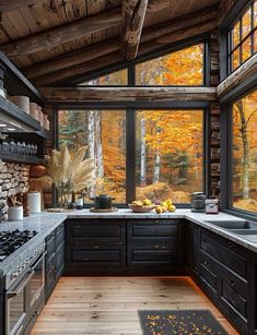 a kitchen with wood flooring and black cabinets in front of a large window that looks out onto the woods