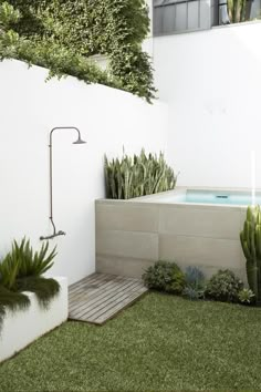 an outdoor hot tub surrounded by greenery and shrubbery in a white walled backyard