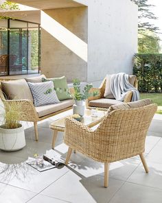 a living room with wicker furniture and plants on the floor outside in front of a house