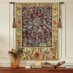 a large tapestry hanging on the wall above a table with books and vases in front of it