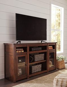 a flat screen tv sitting on top of a wooden entertainment center next to a window