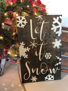 a wooden sign that says let it snow next to a christmas tree with lights and decorations