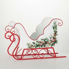 a red sleigh decorated with holly and mist on the top, sitting in front of a white wall