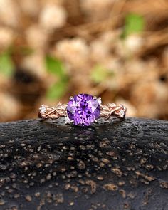 a ring with a purple stone in the center on top of a rock, surrounded by grass and dirt