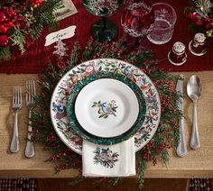 a christmas table setting with silverware, holly and red berries on the placemat