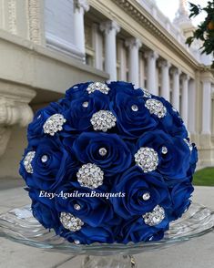 a blue bridal bouquet sitting on top of a glass plate in front of a building