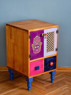 a colorful wooden cabinet with hamsa hand painted on the front and sides, sitting on top of a hard wood floor