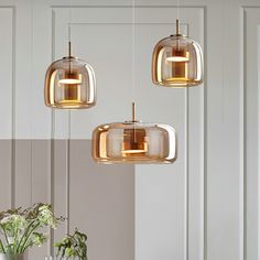 three lights hanging from the ceiling above a dining room table and chairs with flowers in vases