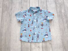 Seaside print short sleeve shirt in 100% cotton fabric featuring a cute seaside print on a pale blue background.  The shirt has a mandarin collar and is fastened at the front with white buttons.  Size range 0-7 years. Great little shirt for casual or occasion wear. Please see sizing in photos for body measurements of the shirt,  if in doubt please do not hesitate to contact me. Care instructions: warm washing cycle, cool tumble dry, iron  My garments are individually handmade. All seams are  fin Cotton Character Print Tops For Beach, Cotton Character Print Beach Top, Beach Cotton Top With Character Print, Cotton Beach Top With Character Print, Light Blue Cotton Short Sleeve Shirt For Summer, Collared Cotton T-shirt For The Beach, Collared Cotton Beach T-shirt, White Character Print Tops For Beach, White Beach Tops With Character Print