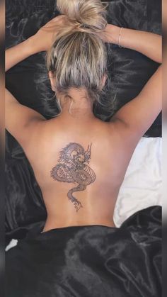 a woman laying in bed with her back turned to the camera and tattoos on her body