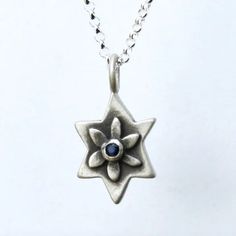 This sterling Star of David necklace departs from convention by featuring a flower at its center that cradles a set stone of your choice. Patina brings out the details of the design and helps make it a striking gift for a Bat Mitzvah or for any age. It hangs on a 16" fine gauge sterling rolo chain (optional longer chain length available through the drop-down menu below). Charm is 3/4". Handmade in the USA by Emily Rosenfeld. Please allow 3-5 business days to ship. Shop our full collection of Jew Symbolic Sterling Silver Star Charm Necklace, Sterling Silver Symbolic Necklace With Star Charm, Silver Star Of David Necklace With Gemstone, Spiritual Star-shaped Gemstone Jewelry, Silver Star Necklaces With Birthstone, Silver Star Necklace With Birthstone, Silver Star Birthstone Necklace, Sterling Silver Star Of David For Jewelry Making, Handmade Sterling Silver Star Of David Necklace