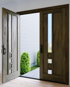 an open door leading to a white house with wooden floors and green bushes on either side