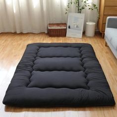 a black futon mattress sitting on top of a wooden floor next to a window