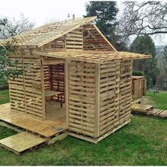 a wooden house made out of pallets in the middle of some grass and trees