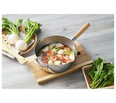 a pan filled with vegetables on top of a wooden cutting board next to other foods