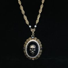 This is a large, circa 1930s, antiqued brass necklace with added brass skull. The large 2 x 1.75 inch pendant has great Victorian elements. The skull on the 1.25 x 1 inch, hematite-colored smooth glass center measures .75 inch and has been added to this vintage necklace. Even the dog tooth prongs holding the center stone in are detailed. It is surrounded by several tiny faux pearls. On the detailed, gold plated scalloped framework are four, .25 inch cut hematite-colored glass stones.  The hemati Gold Metal Necklace For Halloween, Gothic Gold Pendant Necklace, Collectible Gothic Metal Necklace, Nickel Free Gothic Necklaces For Collectors, Nickel-free Gothic Necklaces For Collectors, Gothic Bronze Jewelry With Antique Finish, Gothic Nickel-free Necklaces, Ornate Nickel-free Bronze Jewelry, Elegant Black Jewelry With Antique Finish