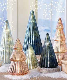 several small christmas trees are sitting in the snow near a window with lights on them