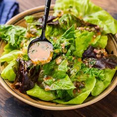 a salad with lettuce and dressing in a wooden bowl on top of a table