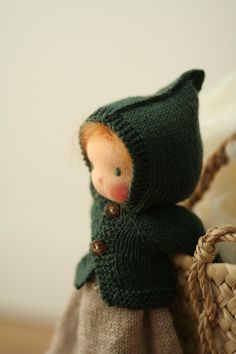 a doll is sitting in a basket with a green coat on it's head