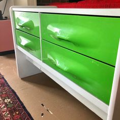 a green and white dresser sitting on top of a floor next to a red rug