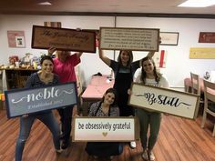 four women holding up wooden signs in a room