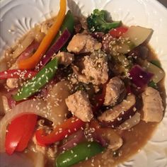 a white plate topped with chicken and veggies covered in sesame seed flakes