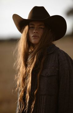 a woman with long hair wearing a cowboy hat and looking off to the side in an open field