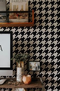 a desk with a computer, books and pictures on top of it in front of a black and white checkered wall