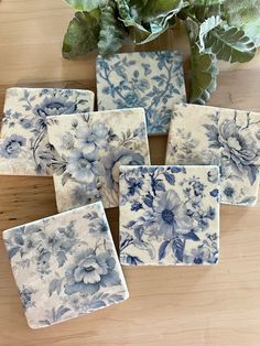 six blue and white flowered coasters sitting on a table next to a potted plant