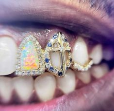 a woman's mouth with two gold rings on top of it and an opal cross in the middle