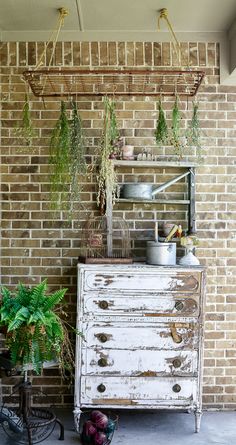 an old dresser with potted plants hanging from it's sides in front of a brick wall