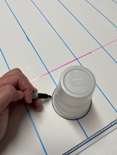 a person is writing on a piece of paper with a marker and a cup lid