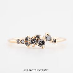 two black and white diamonds are on top of a yellow gold engagement ring, with three smaller stones in the middle