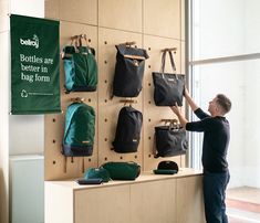 a man standing next to a wall with bags hanging on it's sides and another person reaching for the bag