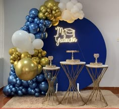 balloons and cake stand in front of a blue backdrop with gold accents for a celebration