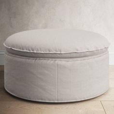 a white round ottoman sitting on top of a hard wood floor next to a wall